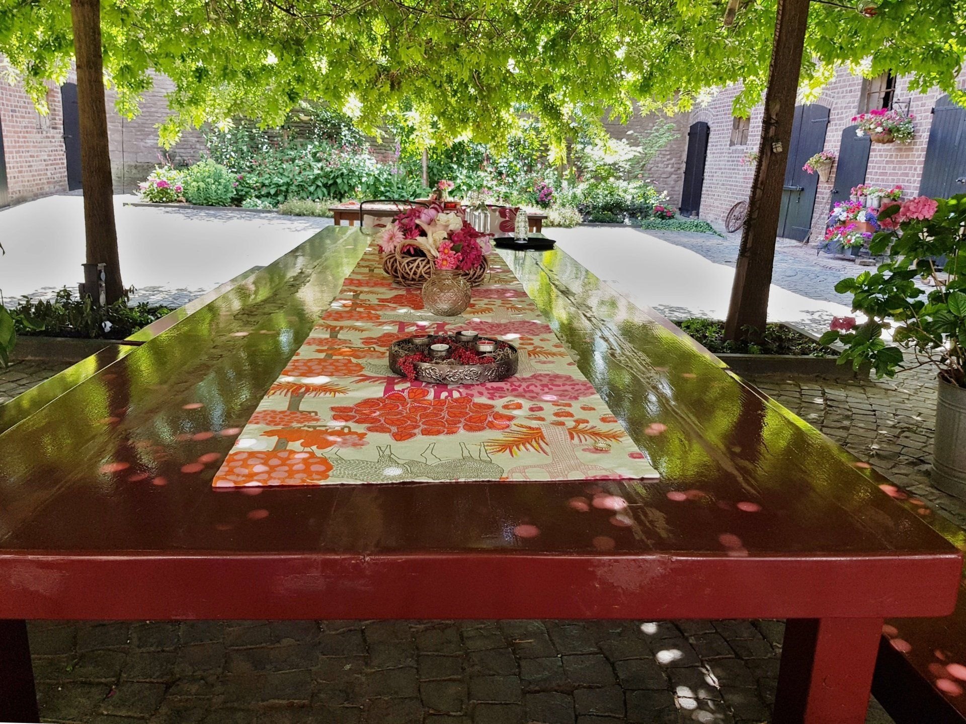 Tafel met bloemen onder het groene bladerdak op het terras van Bonvert